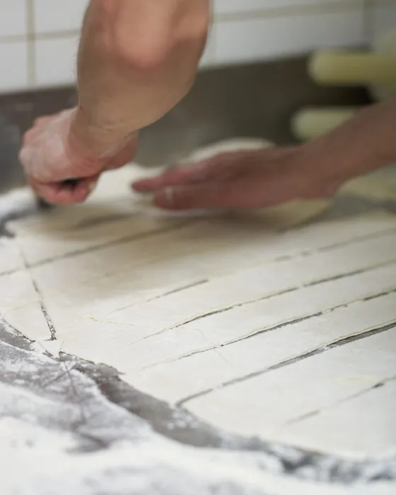 Le mani che tagliano l'impasto della pizza in teglia alla Pizzina