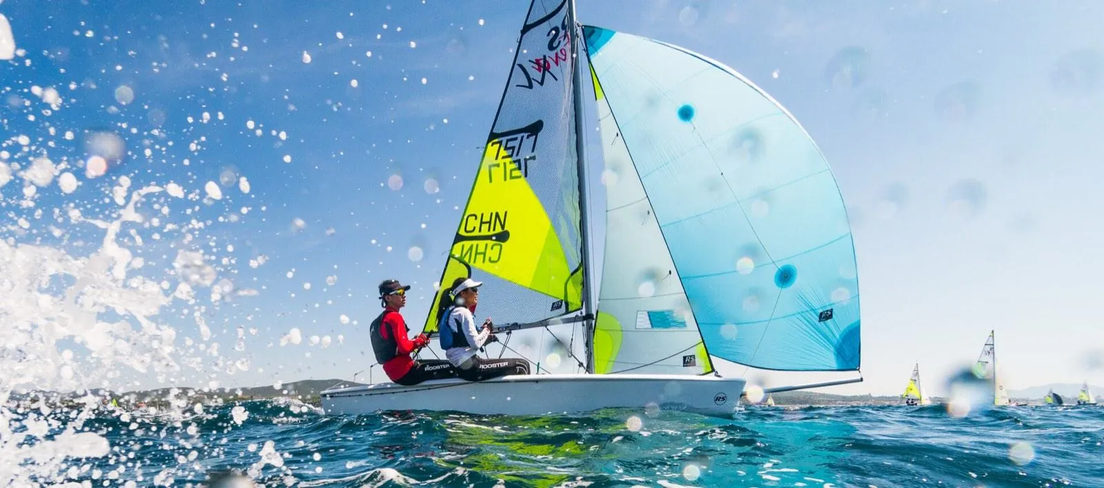Equipaggio di un RS Feva con lo spinnaker aperto, fotografato a pelo d'acqua tra gli spruzzi